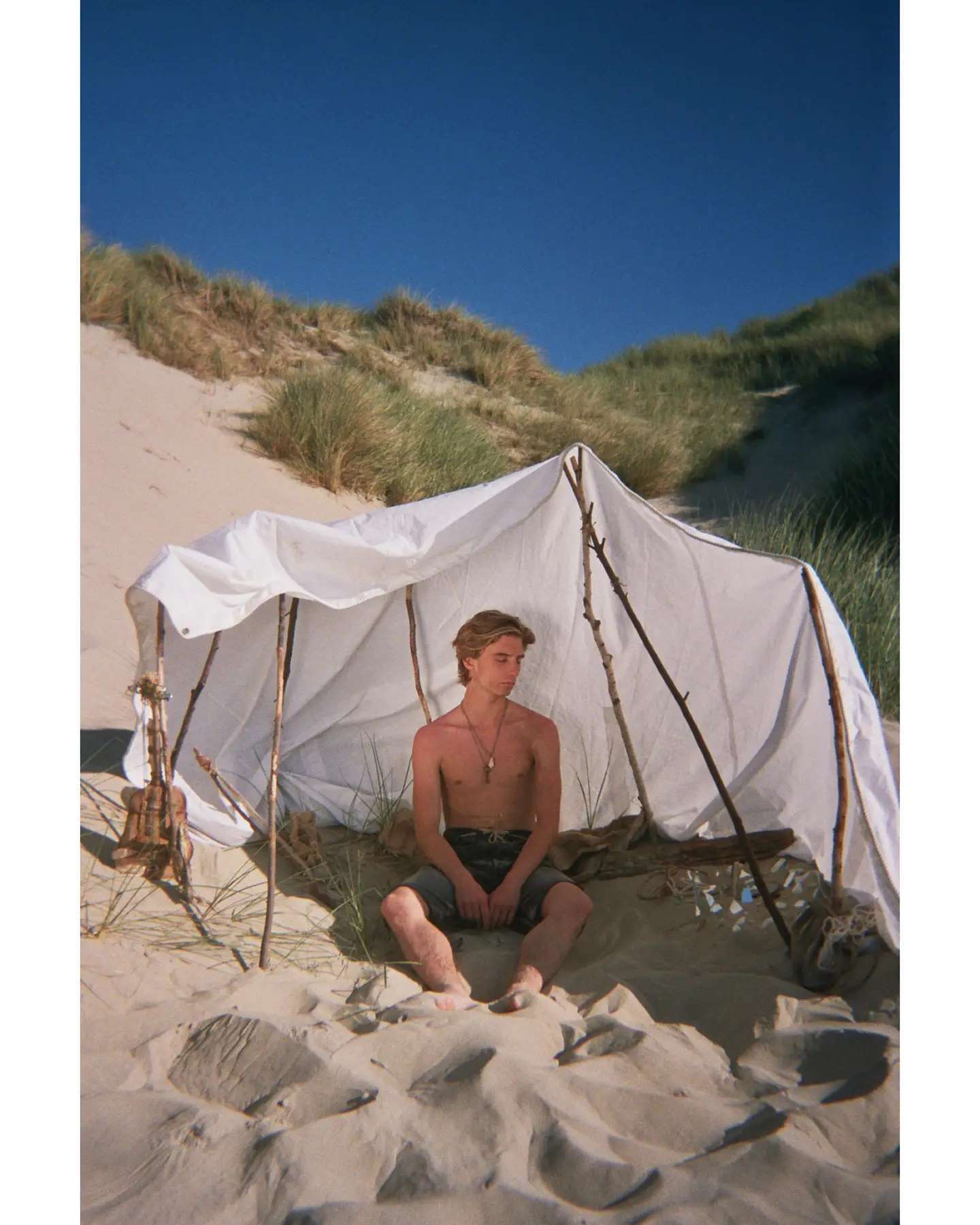 Abel devant un abri de tissu dans les dunes.